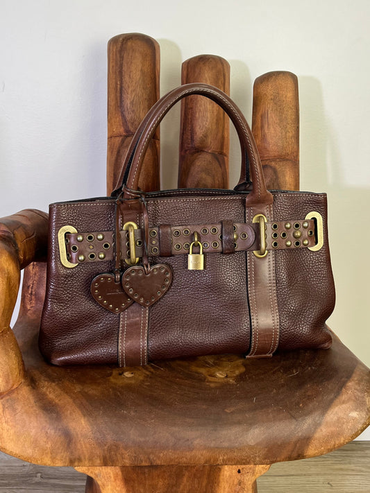 Close-up of vintage Luella Stevie Tote in brown leather showing padlock closure, heart charms, and grommet strap with one missing eyelet.