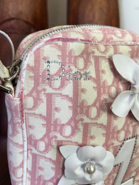 Close-up of Dior rhinestone logo on pink monogram canvas crossbody bag.