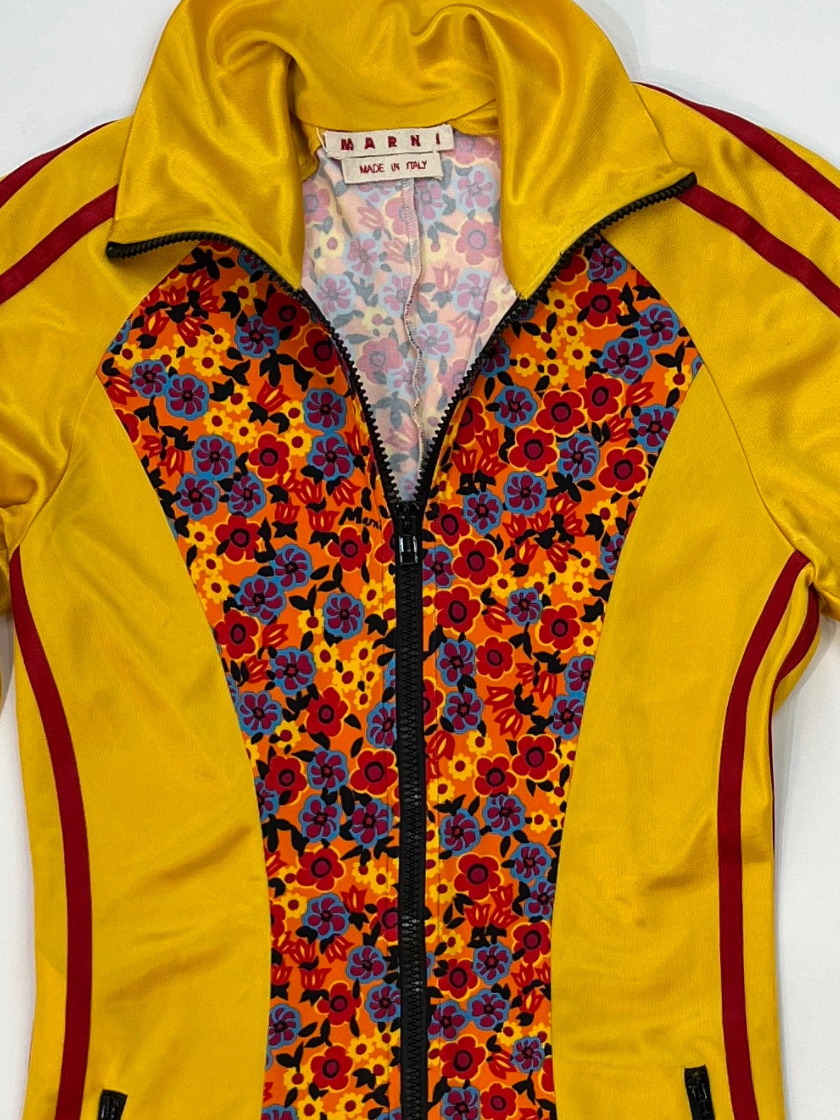Marni yellow zip-up track jacket with multicolor floral panel, red sleeve stripes, high collar, and zippered pockets.