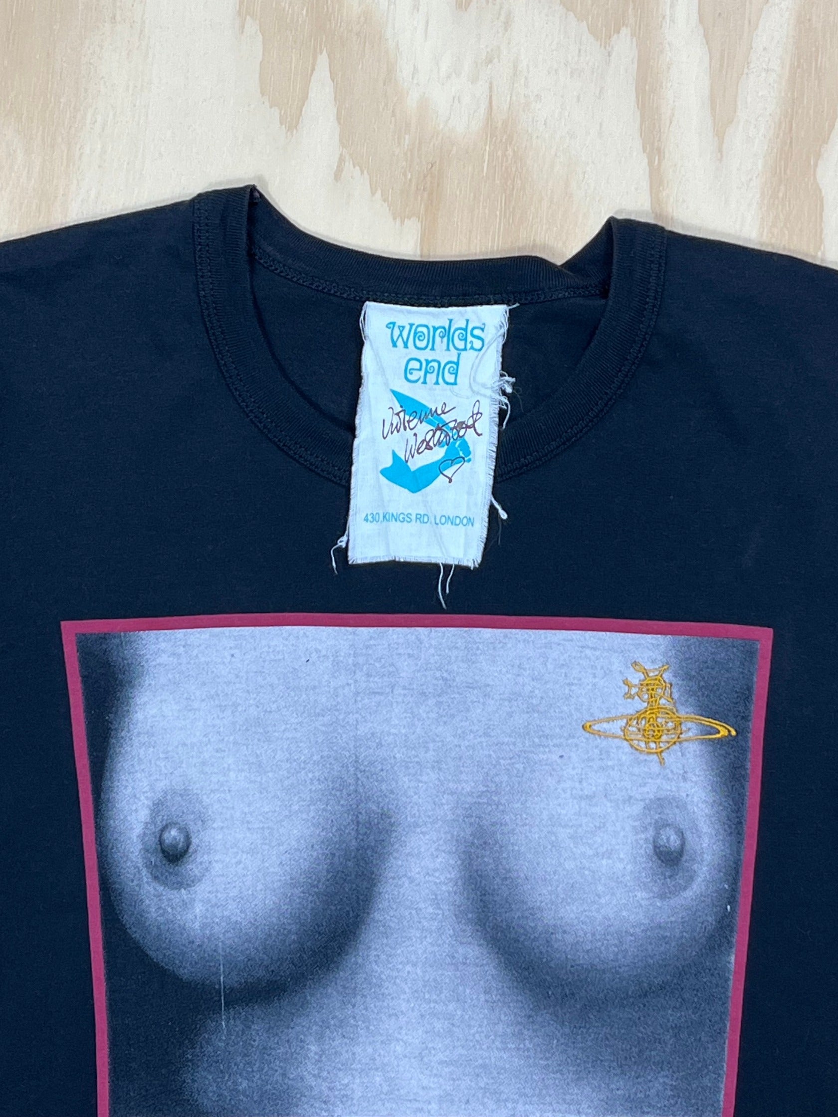 Close up of Vintage Vivienne Westwood Worlds End “Tits” T-shirt in black cotton featuring iconic monochrome chest print framed in red with gold Orb logo, rare 1990s archival piece from Westwood’s first store Worlds End.