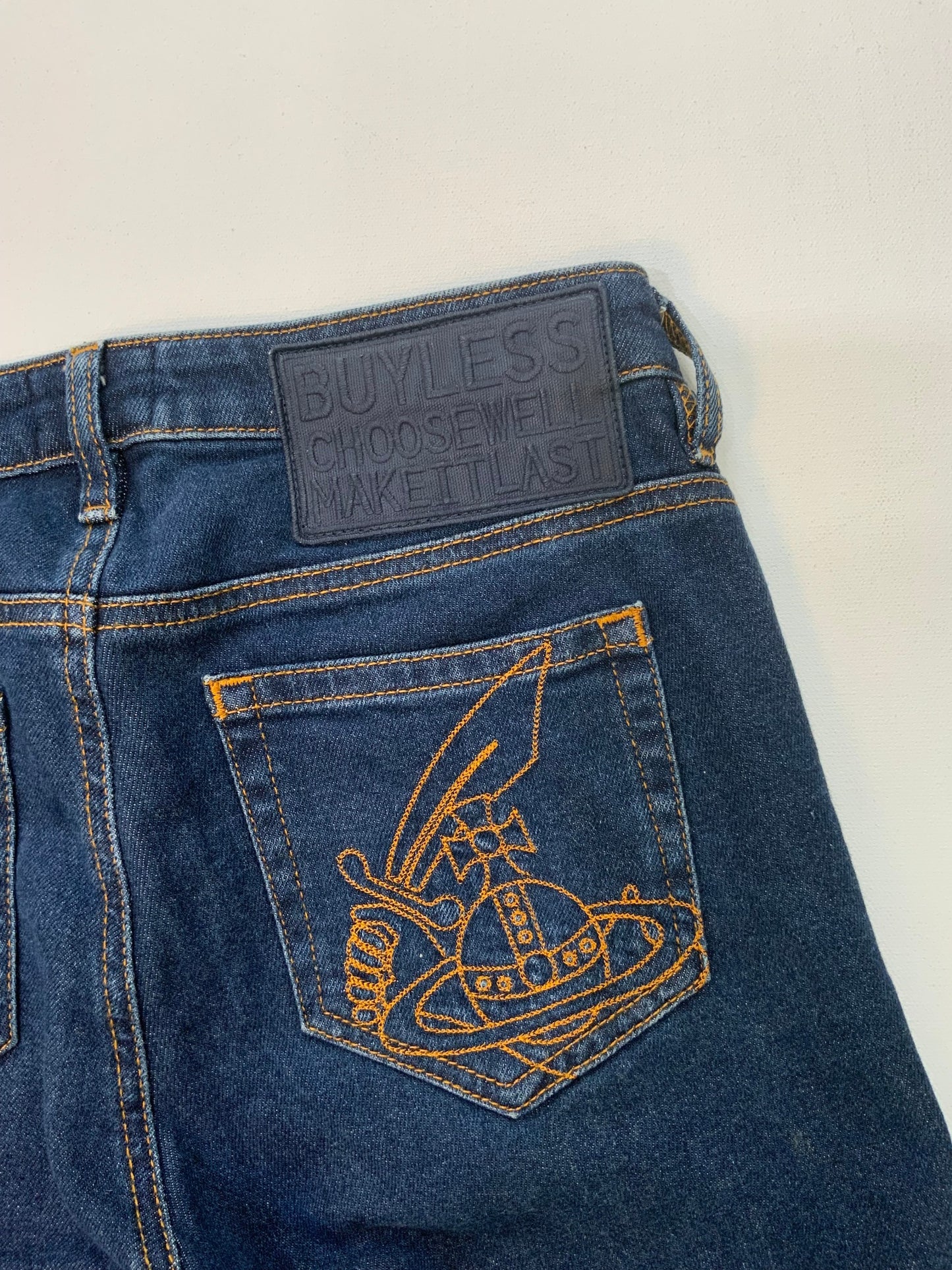 back pocket Vivienne Westwood dark blue skinny jeans with gold Orb embroidery on back pocket and black “Buy Less, Choose Well, Make It Last” patch at waistband. 