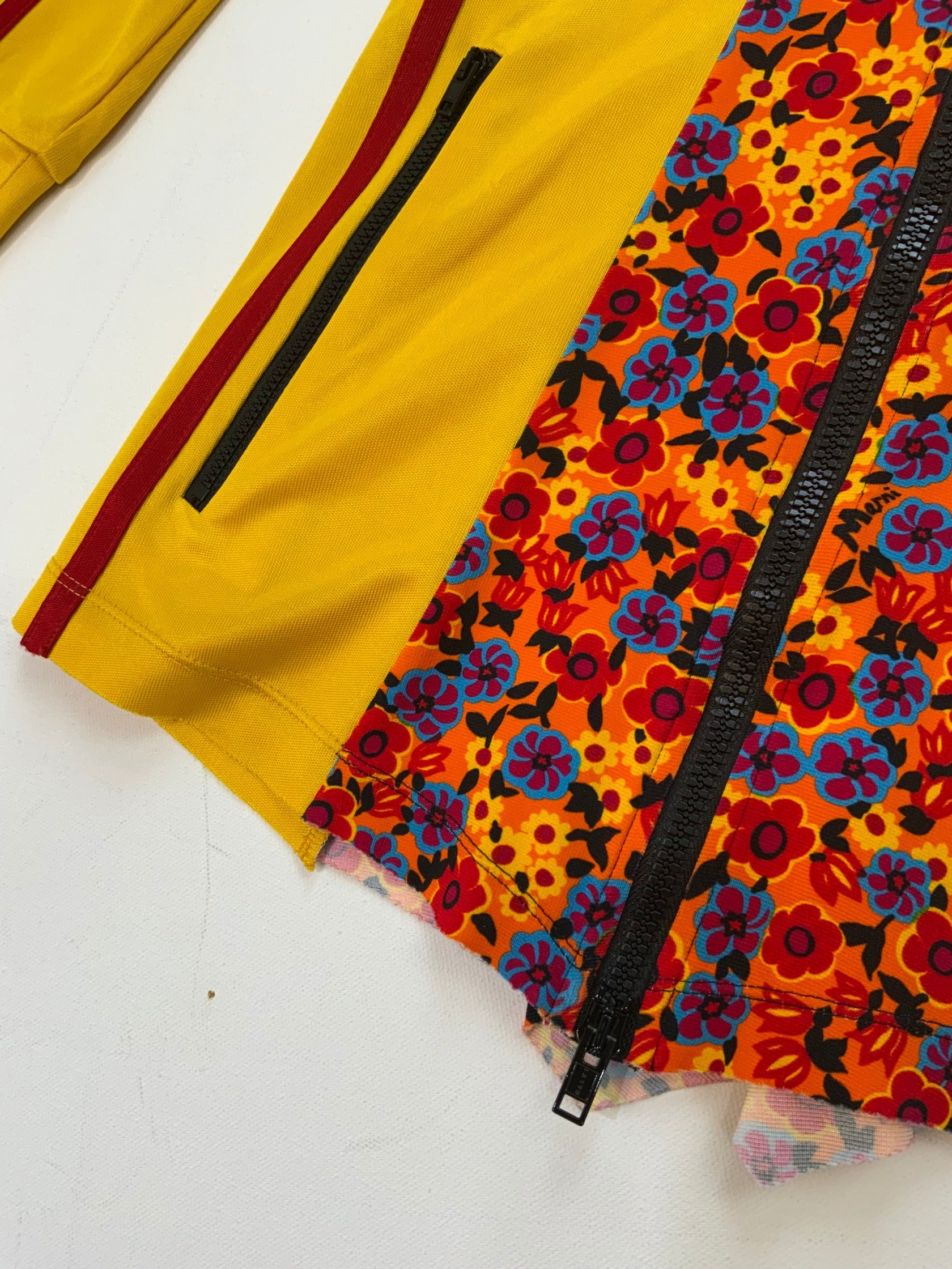 Marni yellow zip-up track jacket with multicolor floral panel, red sleeve stripes, high collar, and zippered pockets.