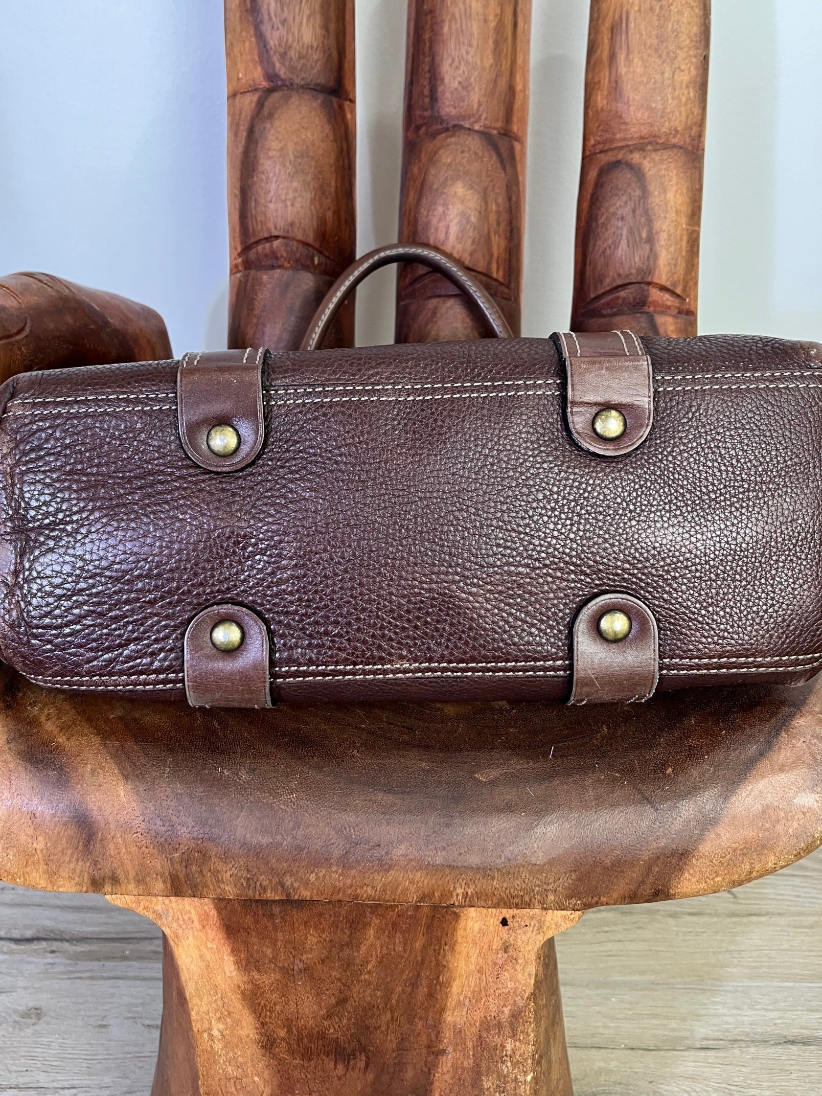 underneath of Close-up of vintage Luella Stevie Tote in brown leather showing padlock closure, heart charms, and grommet strap with one missing eyelet.
