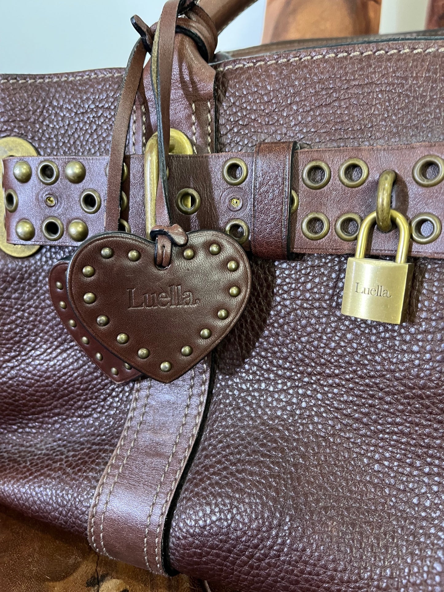 close up of Close-up of vintage Luella Stevie Tote in brown leather showing padlock closure, heart charms, and grommet strap with one missing eyelet.