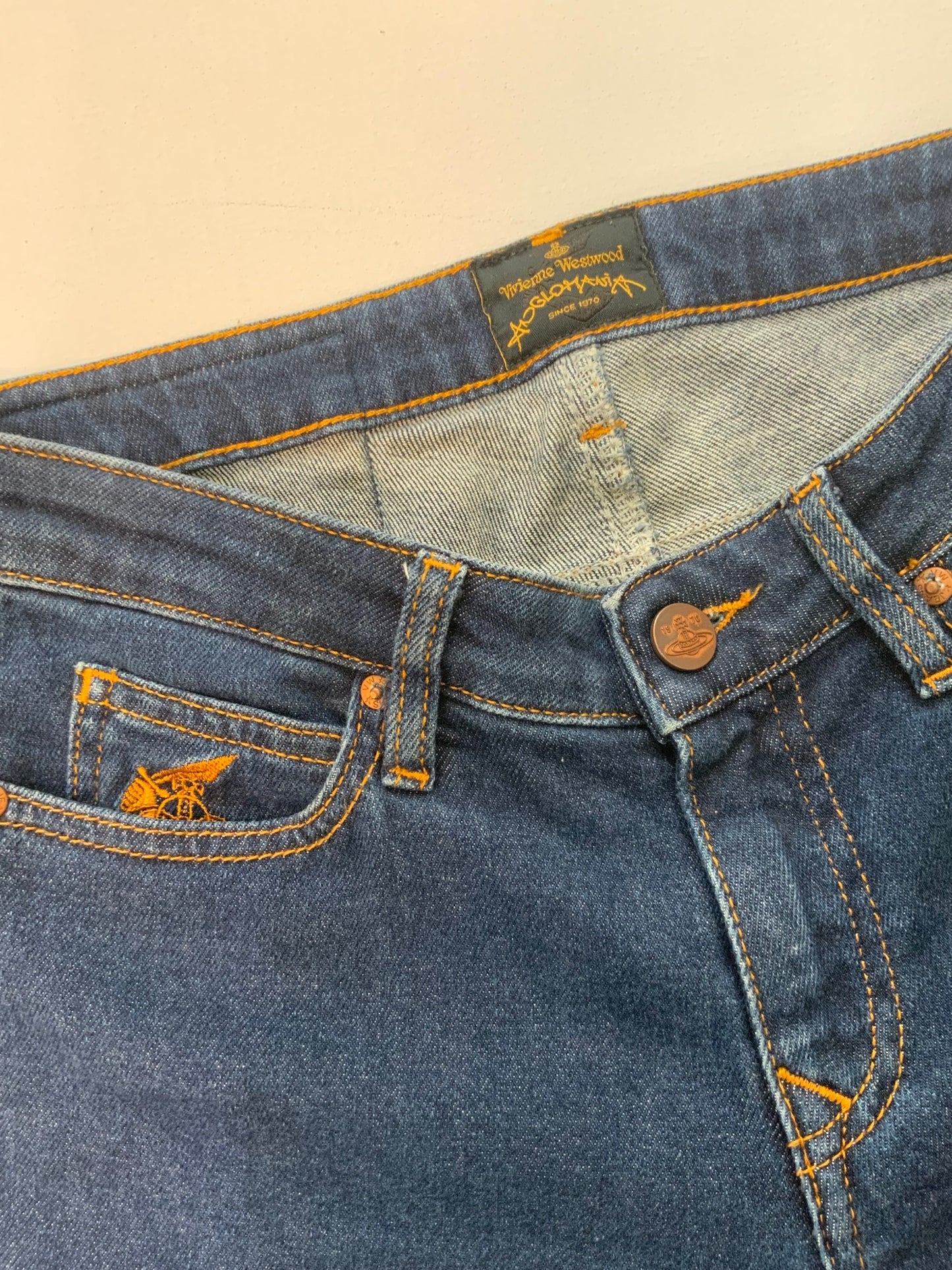 Vivienne Westwood dark blue skinny jeans with gold Orb embroidery on back pocket and black “Buy Less, Choose Well, Make It Last” patch at waistband.