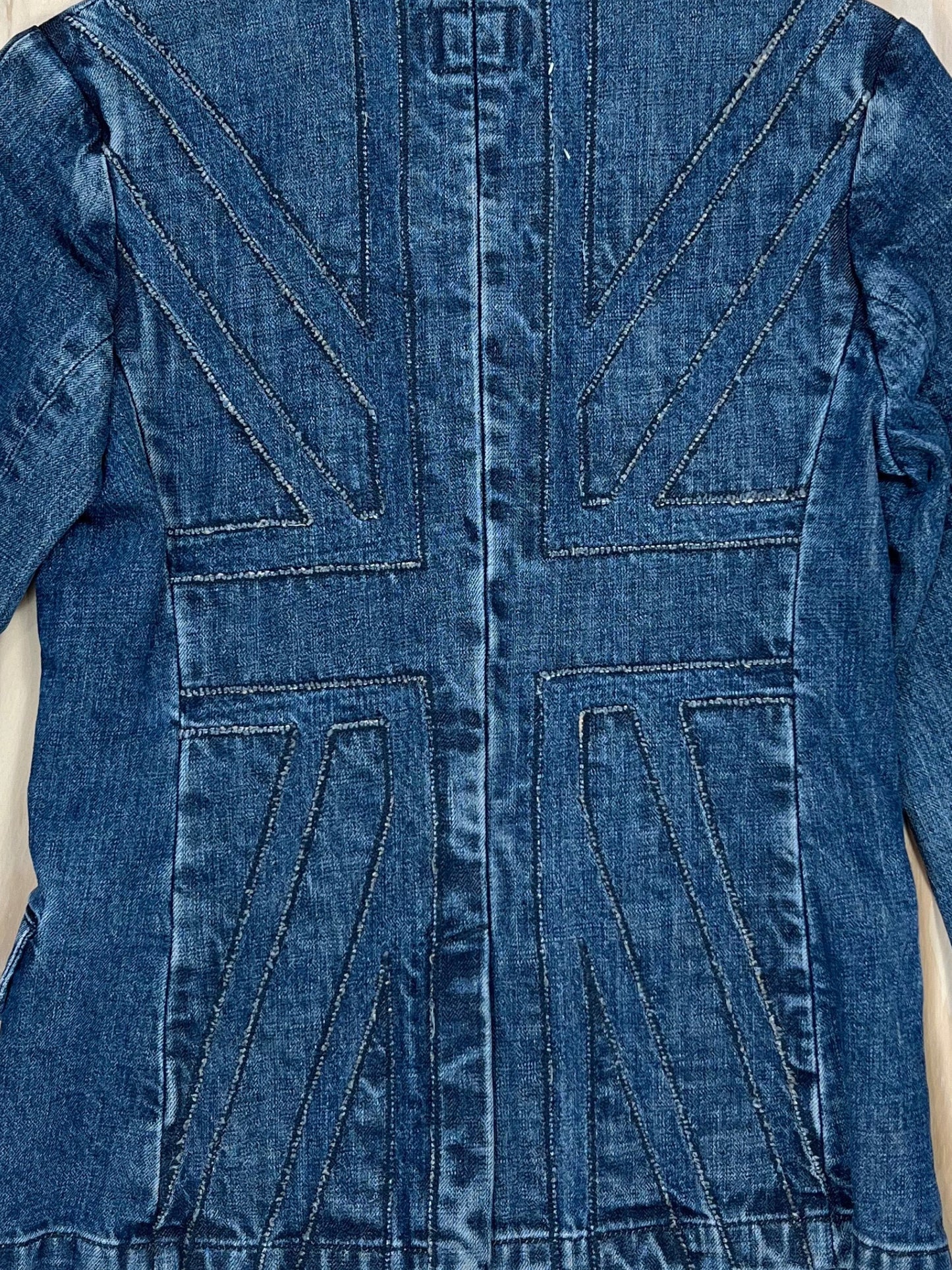 Close-up of Union Jack stitched panel on the back of a vintage denim blazer, washed indigo Y2K tailoring.