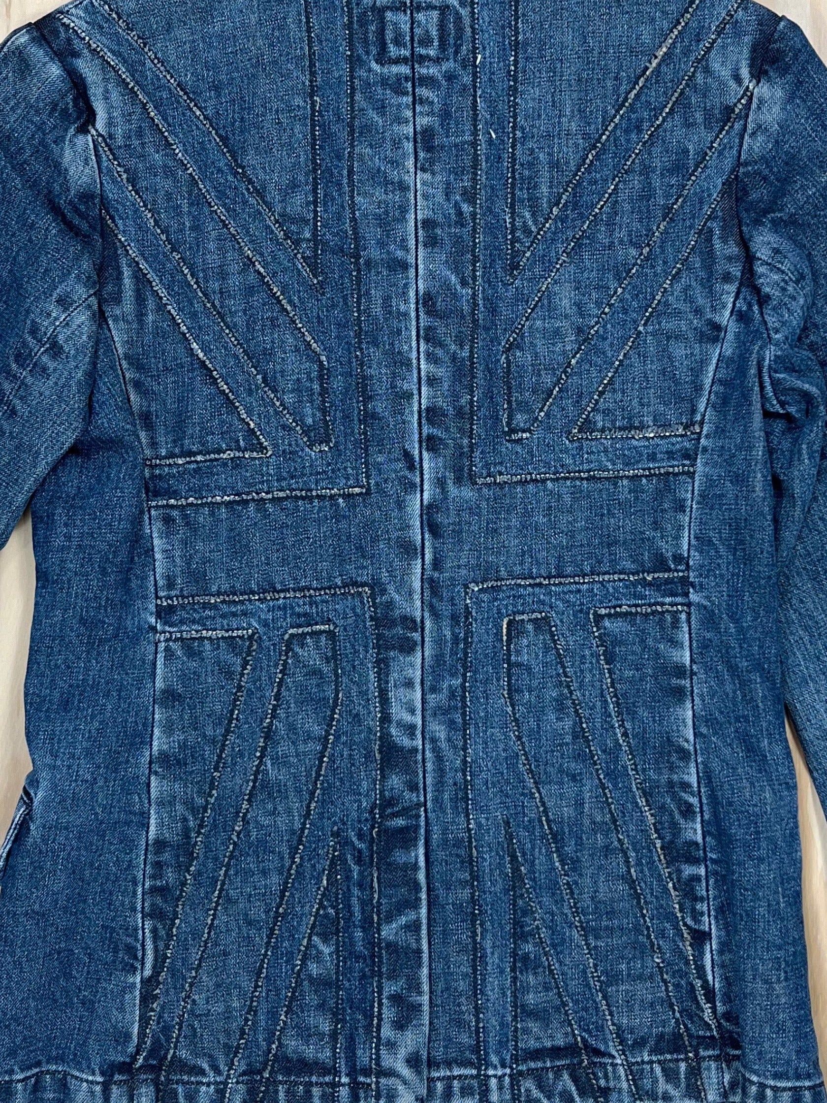 Close-up of Union Jack stitched panel on the back of a vintage denim blazer, washed indigo Y2K tailoring.