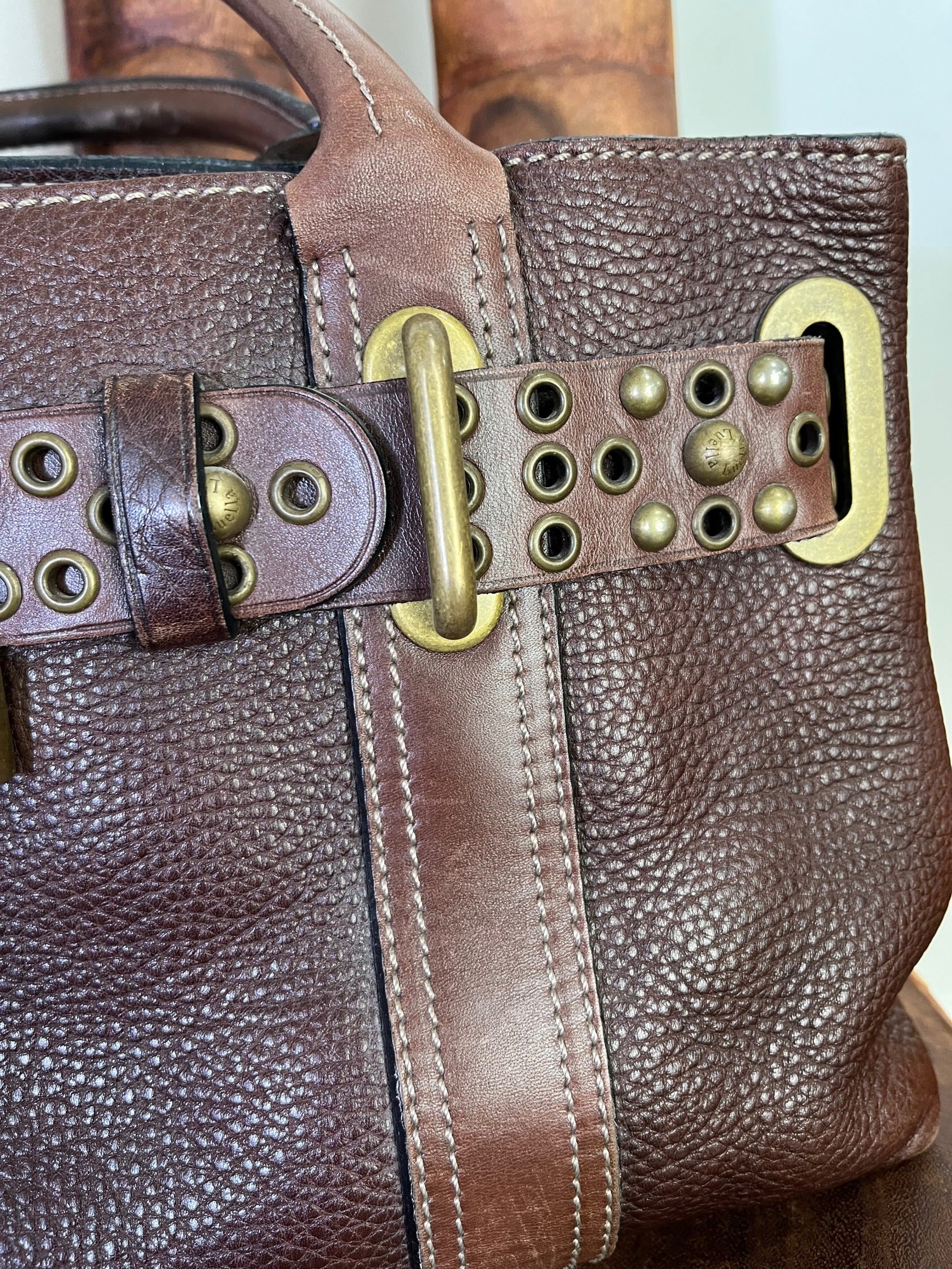 close up of Close-up of vintage Luella Stevie Tote in brown leather showing padlock closure, heart charms, and grommet strap with one missing eyelet.