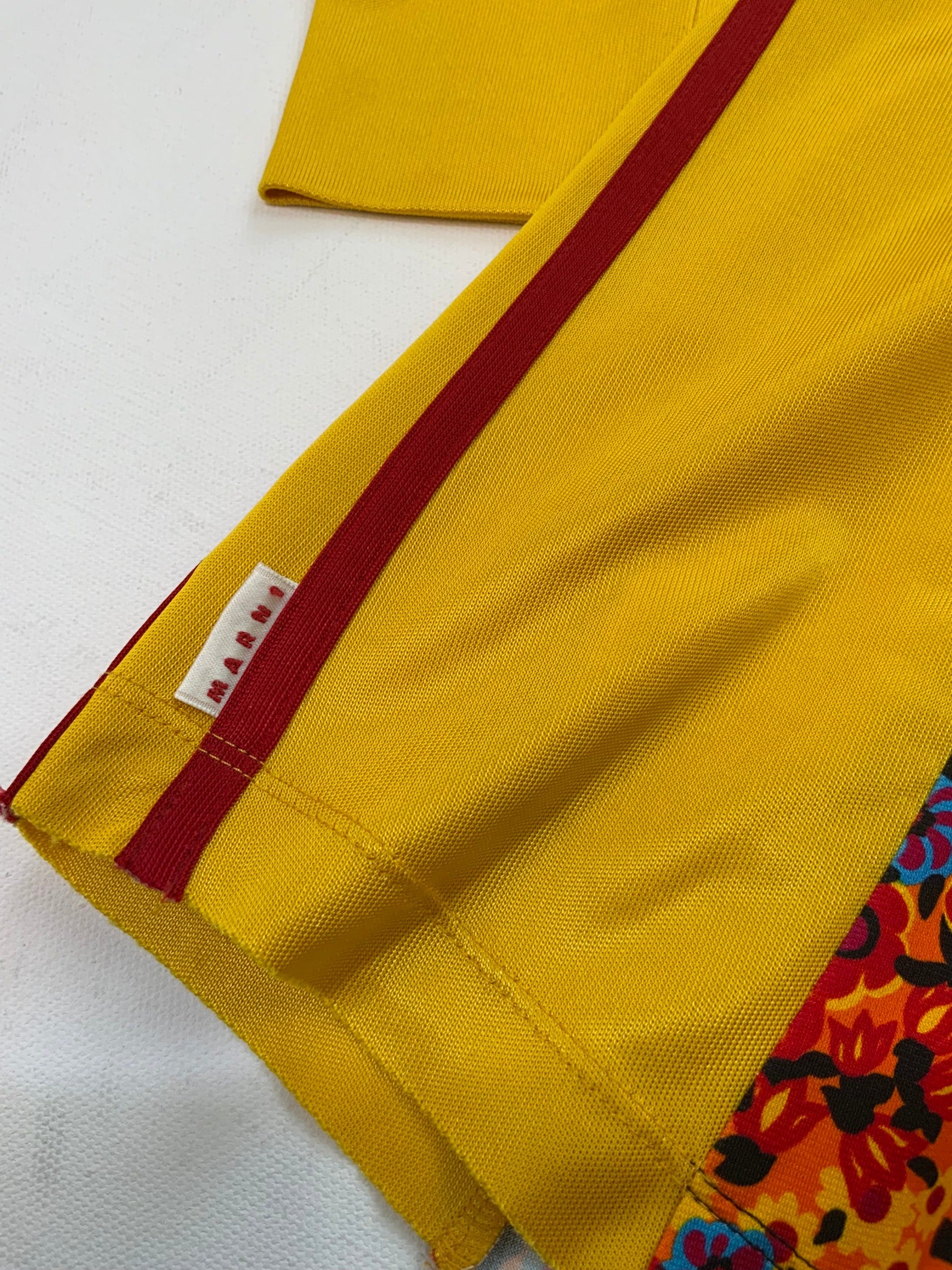 Marni yellow zip-up track jacket with multicolor floral panel, red sleeve stripes, high collar, and zippered pockets.